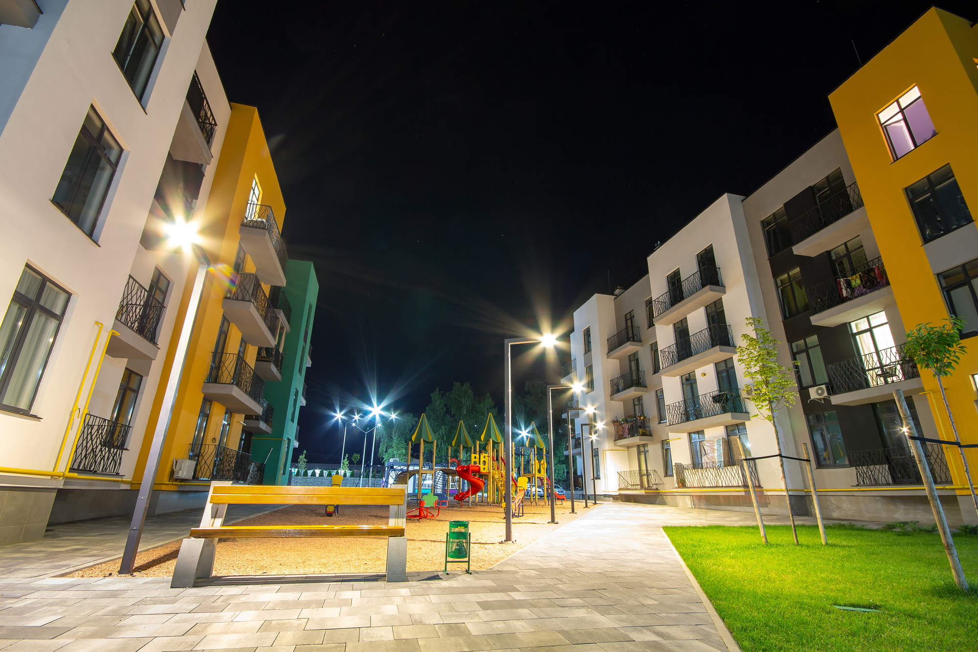 Yard between residential apartment buildings with empty wooden bench and modern flat housing. Real